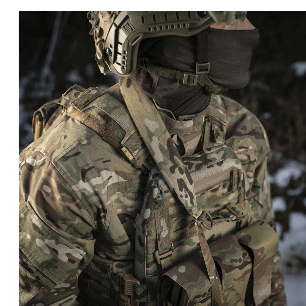 Soldat iført camouflagedragt med taktisk udstyr og M-Tac Universal Våbenrem til geværhåndtering i skovmiljø.