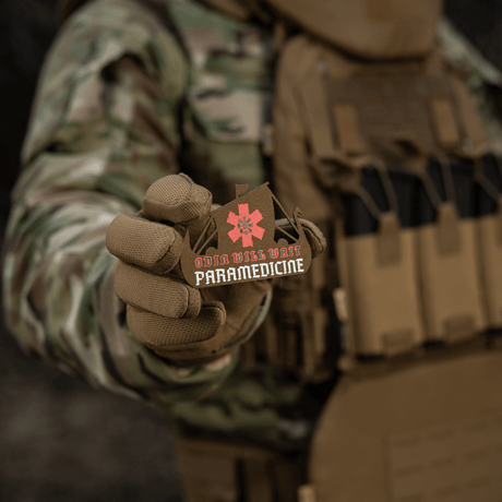 M-Tac Patch Viking Evac i soldatens hånd, viser Odin will wait paramedicine motiv. Camouflage jakke og taktisk vest baggrund.