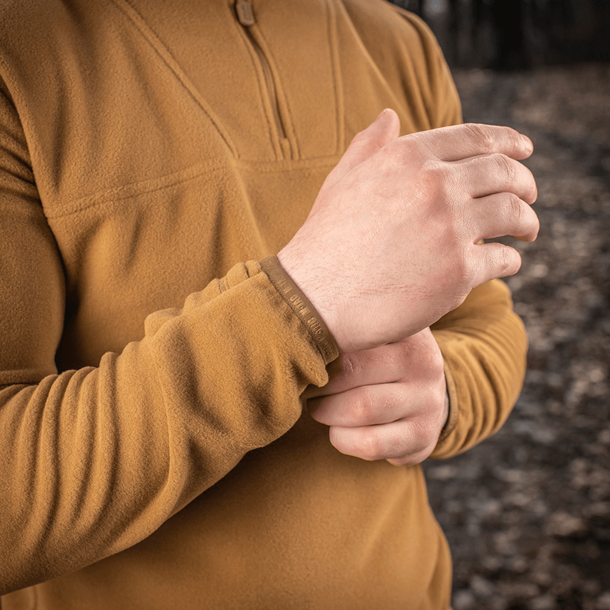 Person iført M-Tac Delta Polartec Fleecejakke i en skov, justerer ærmet for komfortabel pasform, perfekt til kolde dage.