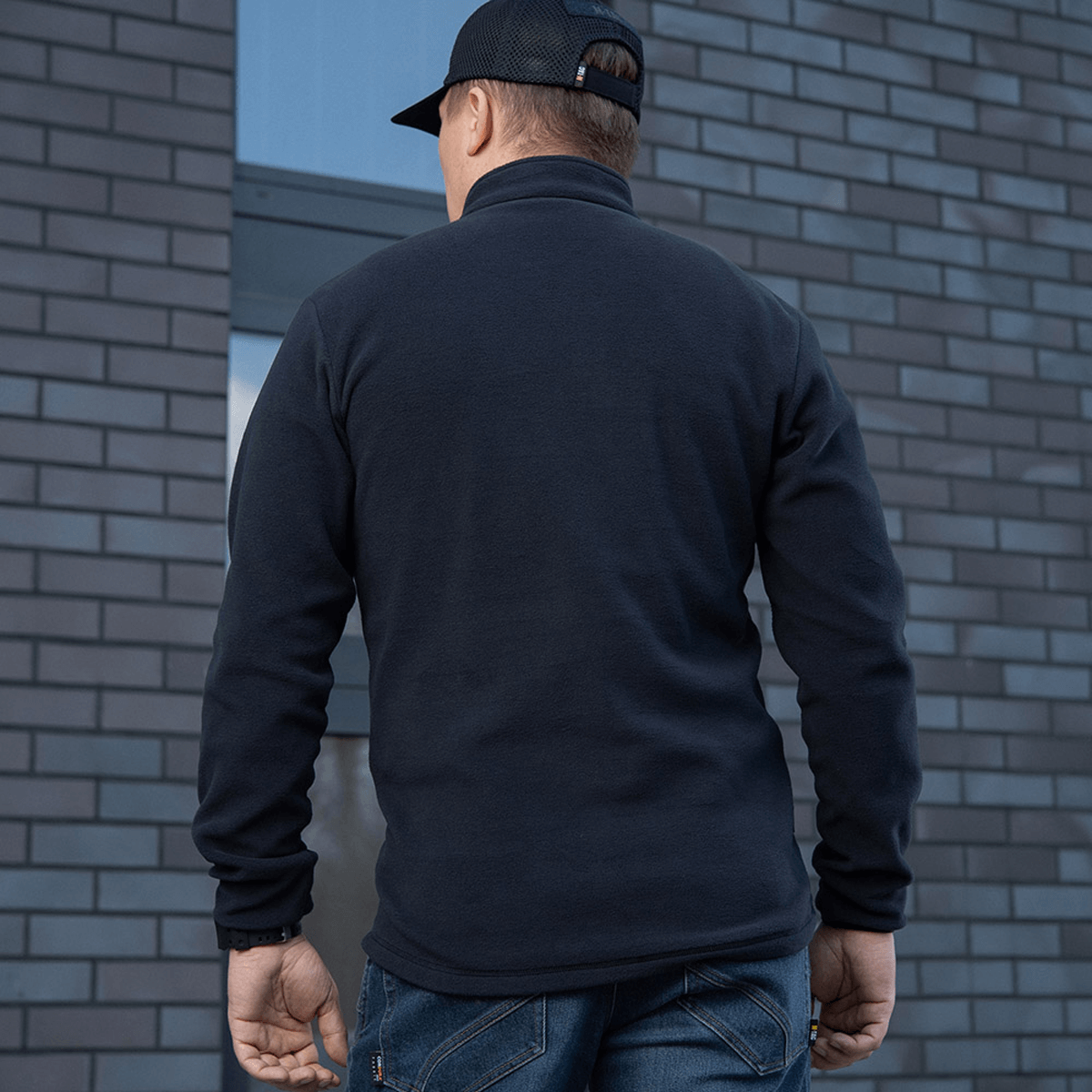 M-Tac Delta Polartec Fleecejakke set bagfra på en person bærer en sort kasket, mod en grå murstensvæg.