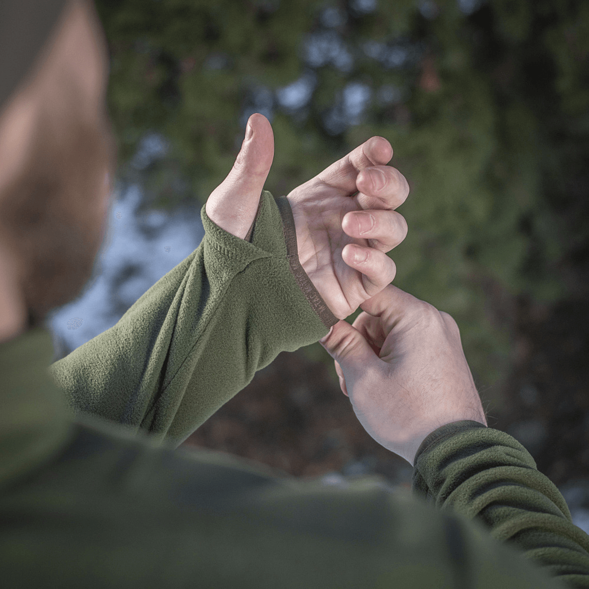 En person iklædt M-Tac Delta Polartec Fleecejakke viser tommelfingerhul i ærmet på vinterdag. Stilfuld og funktionel fleecejakke.