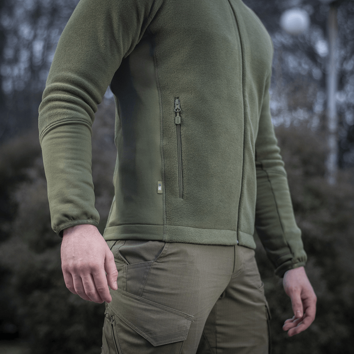 M-Tac Polartec Sport Fleecejakke i grøn, designet til funktionalitet og komfort i forskellige vejrforhold, her vist i brug udenfor.