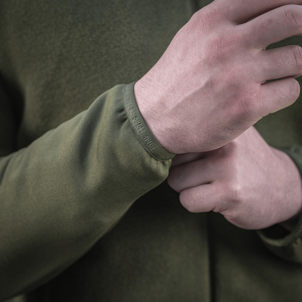 En person justerer ærmet på en M-Tac Polartec Sport Fleecejakke i grøn farve, der viser stoffets tæthed og finish.