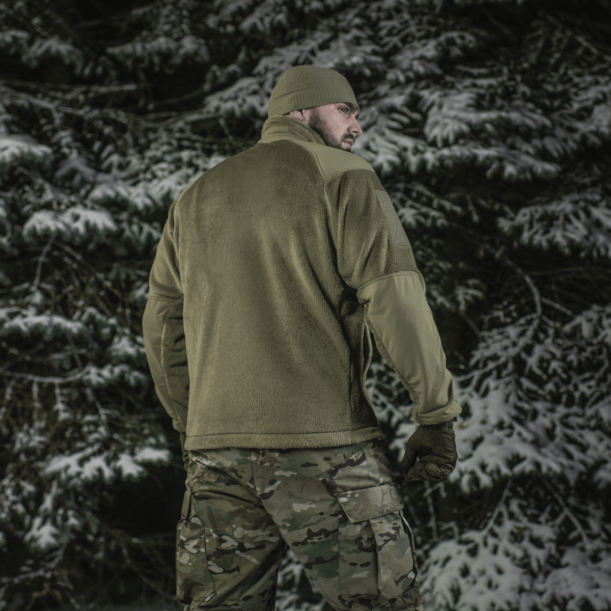 Mand iført M-Tac Battle Fleece Polartec Jakke i sneklædt skov, set bagfra med anatomisk pasform og camouflagebukser.