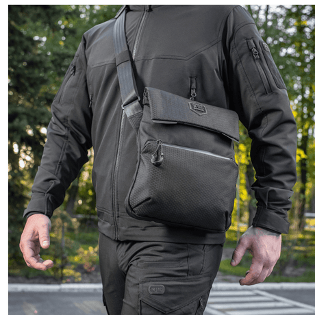 Mand bærer M-Tac Konvert Taske Elite i Cordura materiale, justerbar skulderrem og tablet-design, set udefra i et udendørs miljø.