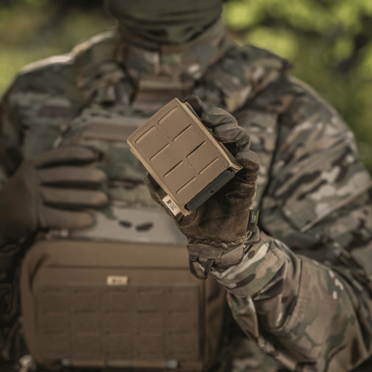M-Tac Magasinlomme med Elastik (10 cm) Laser Cut holdt af taktisk klædt person i skovmiljø, der fremviser holdbarhed og brugervenlighed.