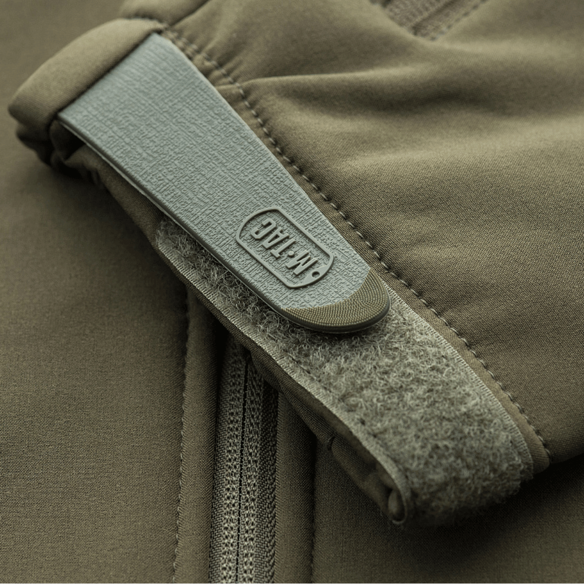 Nærbillede af en M-Tac Soft Shell Police Jakke i beige, der viser lynlås og velcrolukning på ærmet.