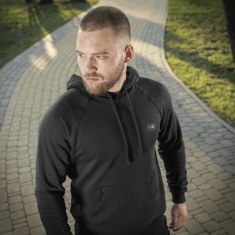 Mand iført M-Tac Hættetrøje Cotton Raglan, komfortabel hverdags- og aktivtøj i 100% bomuld, på sti i grøn park.