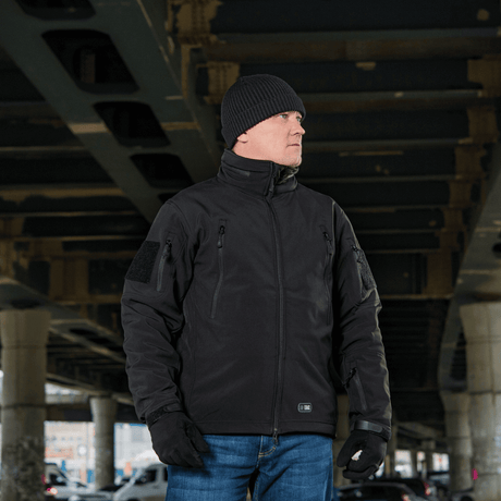 Mand iført M-Tac Soft Shell Jakke med Liner under en bro, praktisk til dårligt vejr med aftageligt fleecefoer.