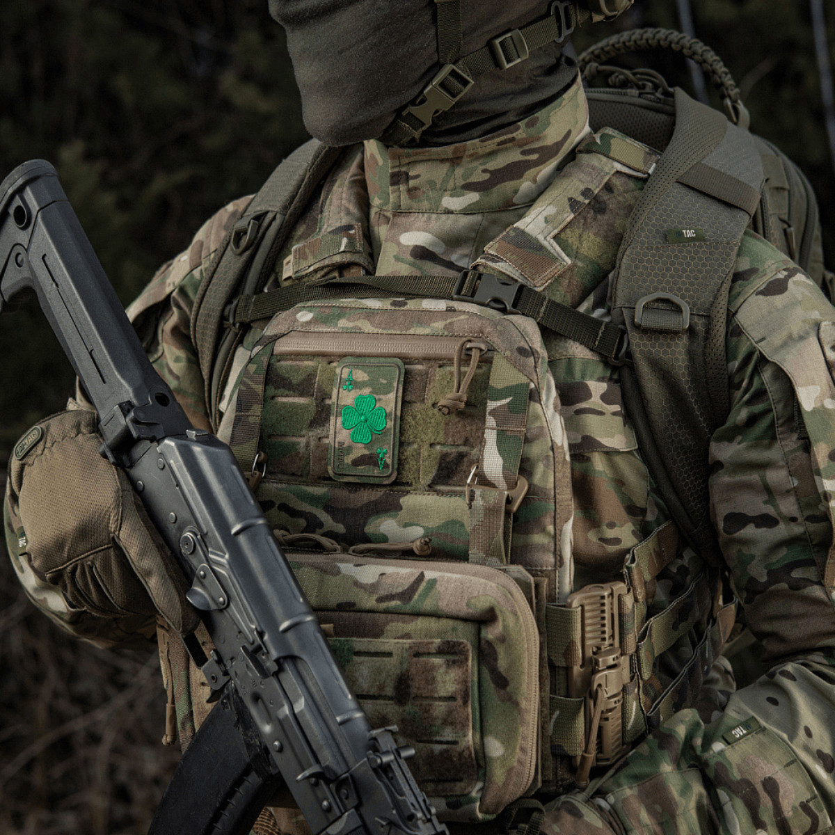 Militærtøj med M-Tac Patch Lucky Card (Broderi) med kløverblad, fastgjort med Velcro til camouflageret rygsæk.