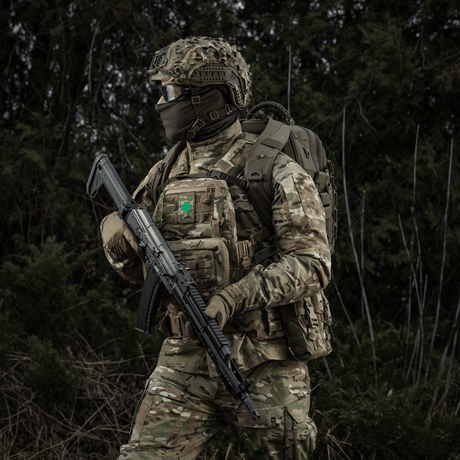 Soldat iført militæruniform med M-Tac Patch Lucky Card (Broderi) fastgjort på vest, symbol på held og beskyttelse, camouflage i skovområdet.