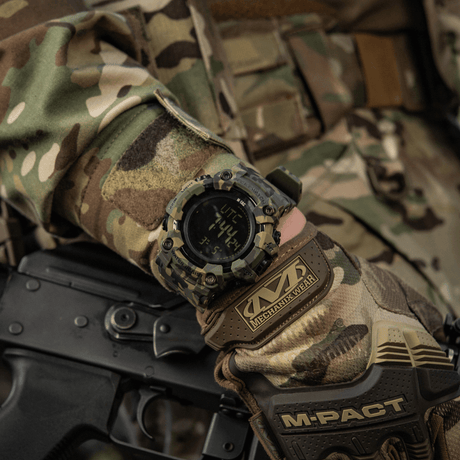 M-Tac Tactical Ur 2037 på camouflagebeklædt hånd, viser robust design med LED-baggrundsbelysning og funktioner til taktisk brug.
