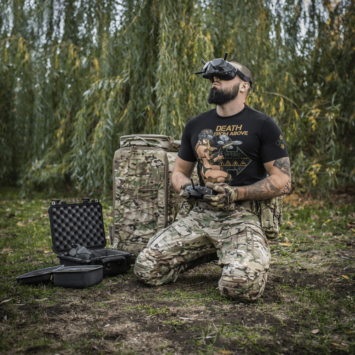 Mand iført M-Tac T-Shirt Delivery Service, inspireret af amerikansk Pin-Up-kultur, styret drone i camouflagetøj i naturen.