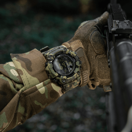 M-Tac Tactical Ur 2037 på håndled med camouflage tøj, ideelt til outdoor og taktisk brug, fremhæver robust design og funktionalitet.