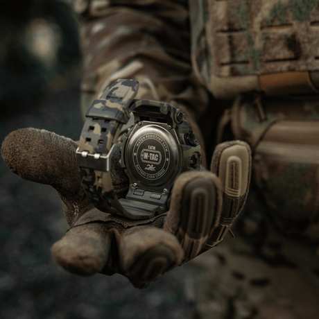 M-Tac Tactical Ur 2037 i camouflagedesign, modstandsdygtig op til 5ATM, holdt af en taktisk handsket hånd i skovmiljø