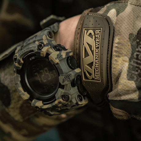 M-Tac Tactical Ur 2037 med robust design, perfekt til outdoor og taktiske aktiviteter, vist på camouflagetøj mod en baggrund af naturfarver.