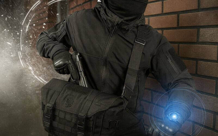 Taktisk klædt person med skuldertaske og lommelygte, står op ad murstensvæg, klar til mission. Effektivitet og beredskab.