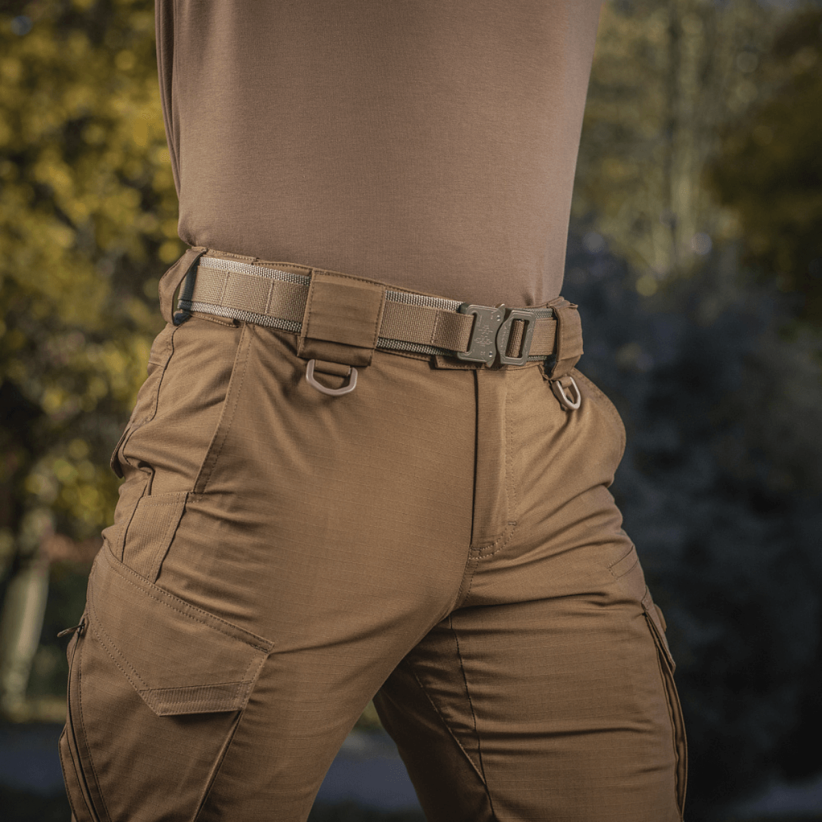 M-Tac Cobra Buckle Taktisk Bælte Laser Cut fastgjort på bukser i udendørs setting, ideelt til militær og politi.