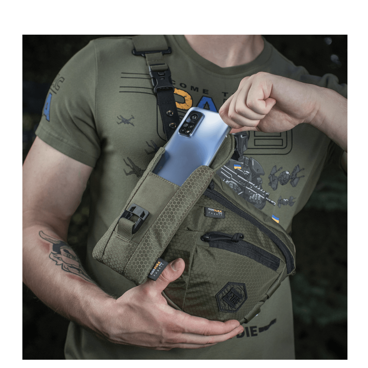 Mand med M-Tac Smartphone Lomme Elite Large Hex i mørkegrøn farve holder en smartphone.