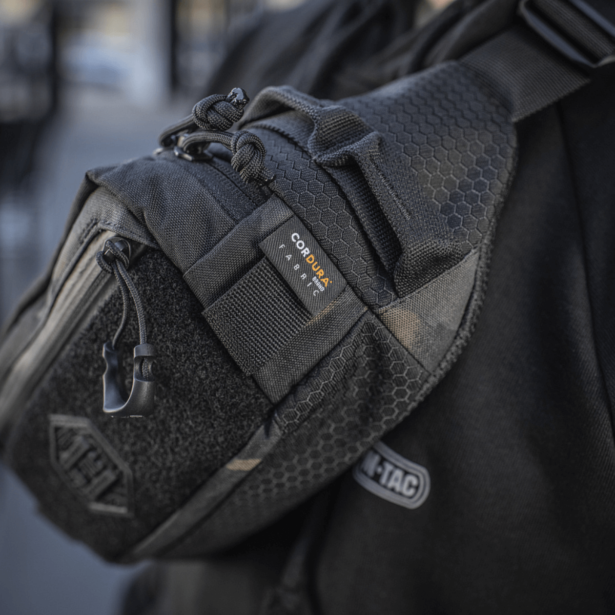 M‑Tac Bæltetaske Elite Hex vises båret af en person, fremstillet i Cordura med YKK lynlåse, ideel til dagligt eller taktisk brug.