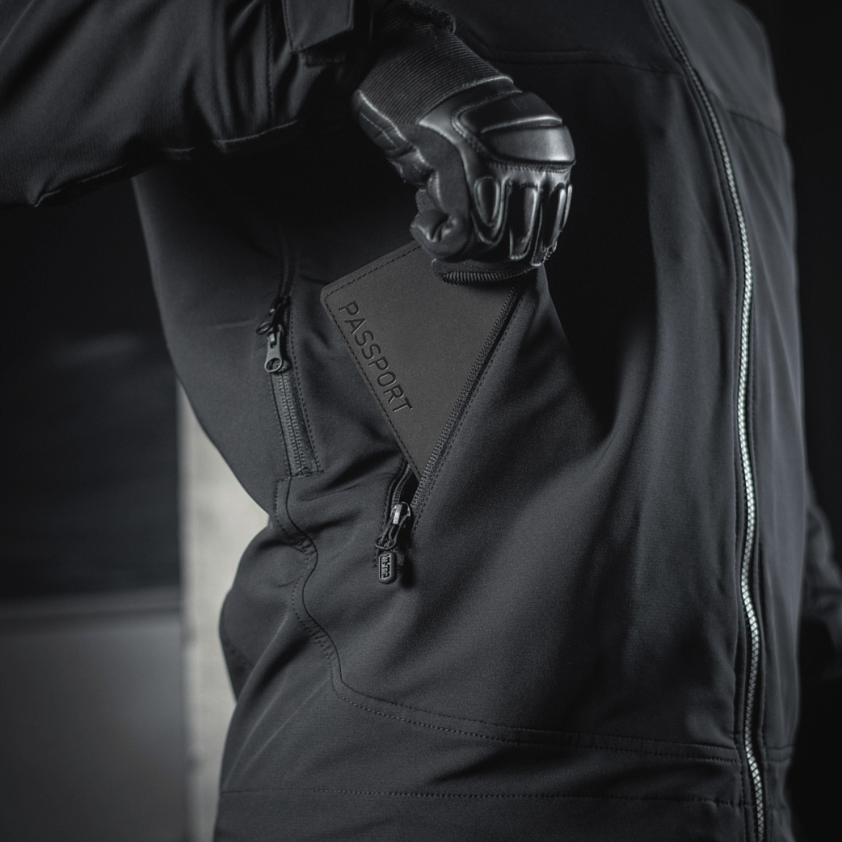 Person i sort jakke holder M‑Tac Pascover med "Passport"-tryk.
