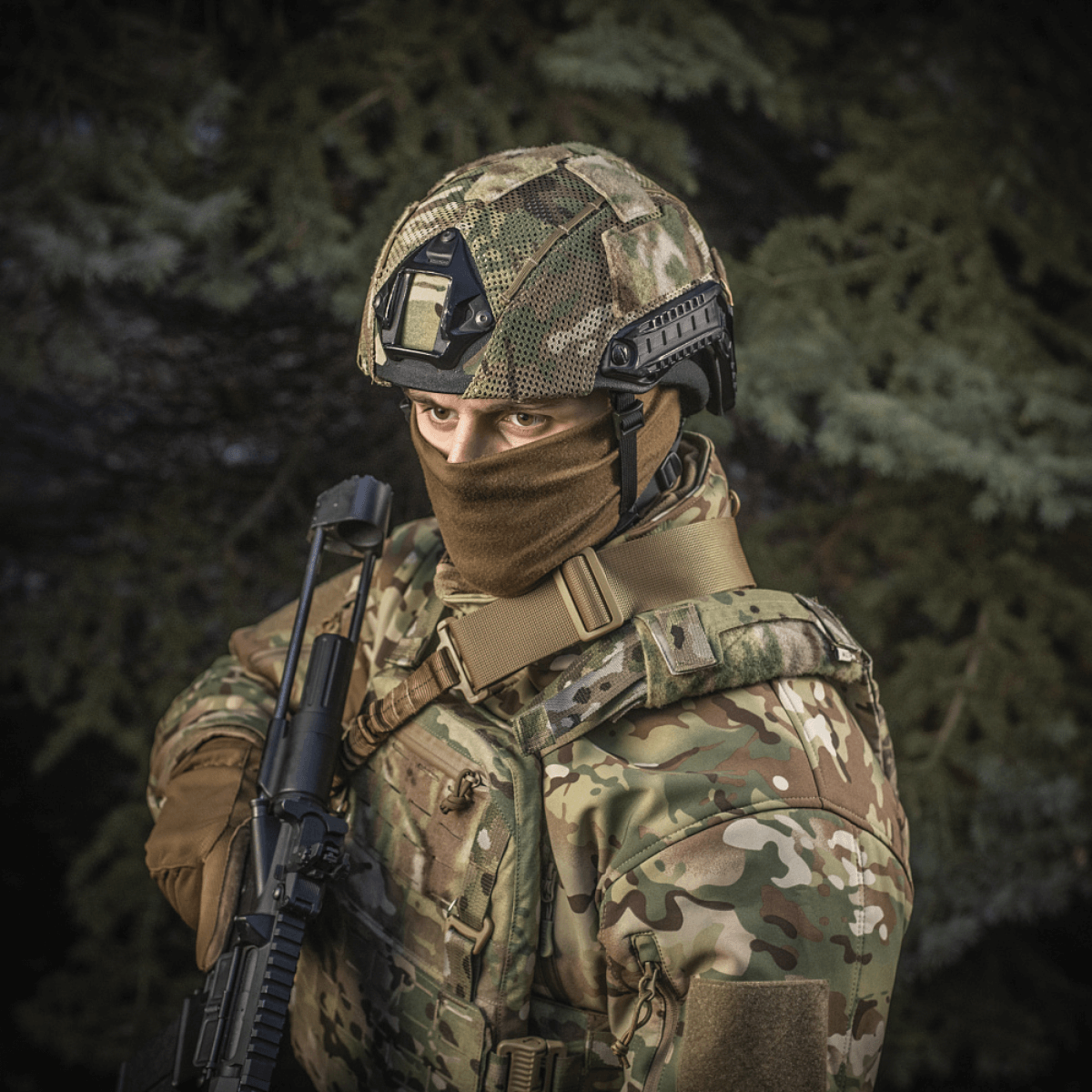 Soldat iført M‑Tac Hjelmcover Shroud Elite i MULTICAM, til TOR-D hjelme, med våben i skovlandskab.