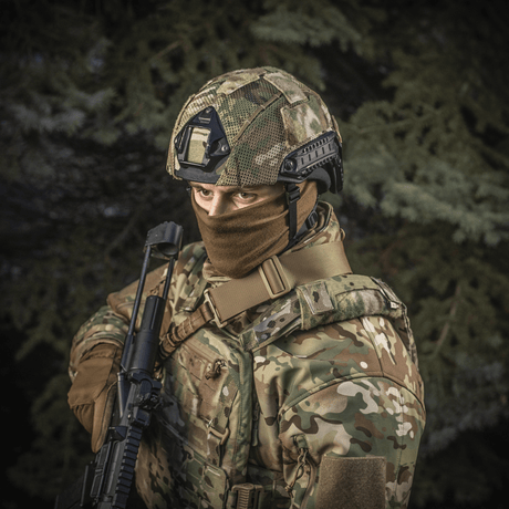 Person wearing M‑Tac Hjelmcover Shroud Elite in MULTICAM, holding rifle, displaying tactical gear outdoors.