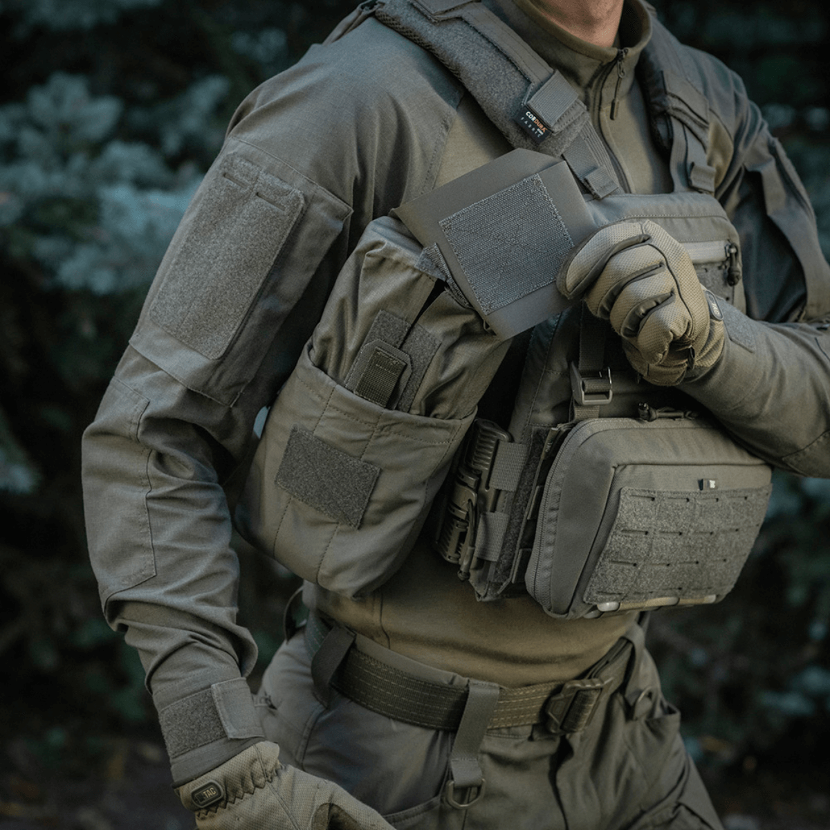 Person wearing tactical gear and holding M‑Tac Medic Pouch Vertical Large Elite in a forest setting.