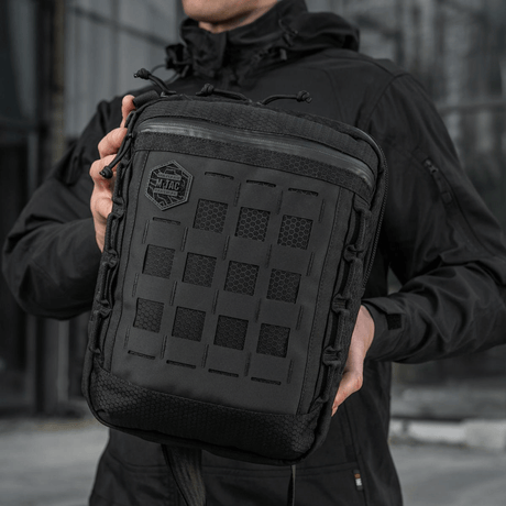 M-Tac Tablet Bag Laser Cut Hex i Cordura stof med Laser Cut MOLLE og hurtig adgang, holdt af en person i sort jakke.