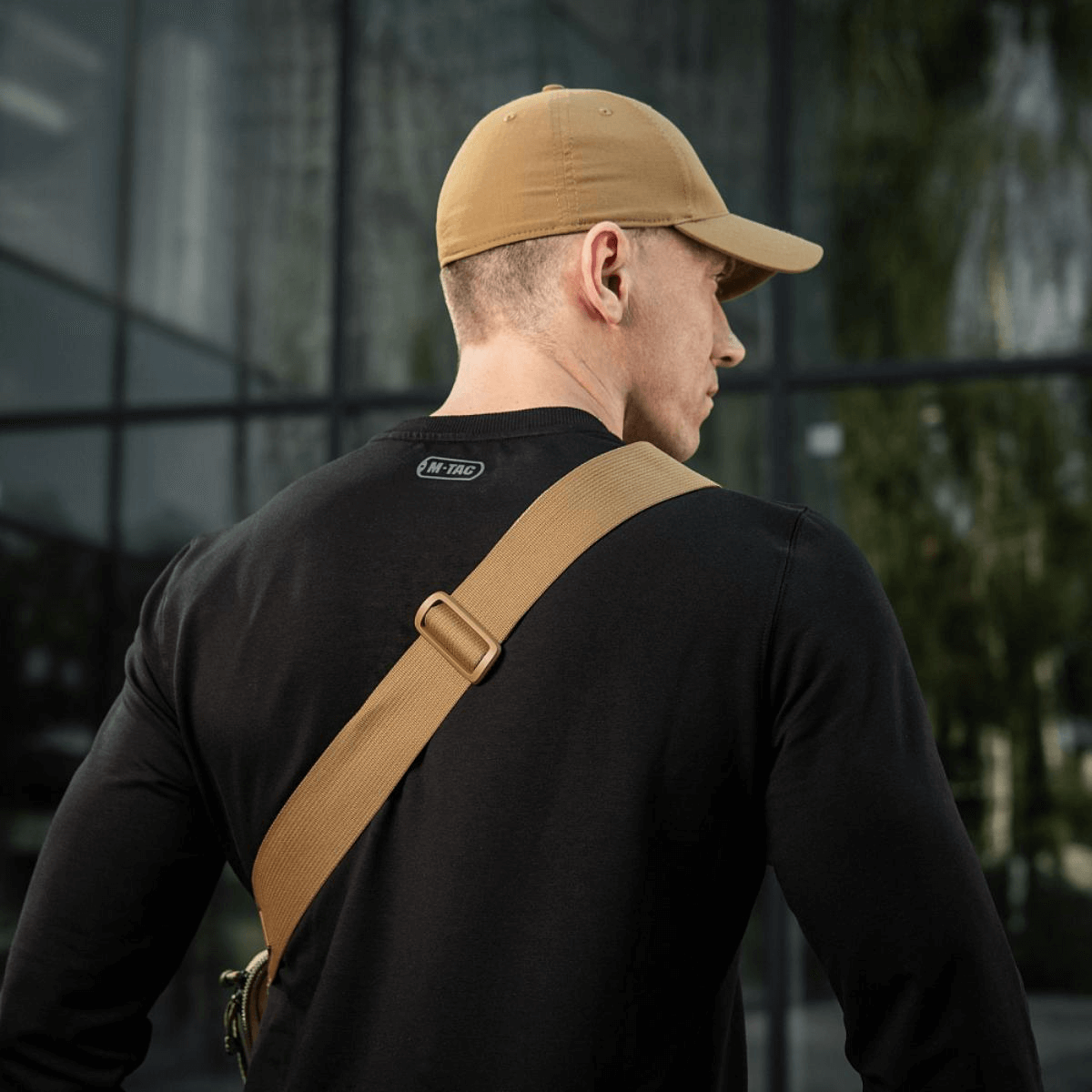 Mand iført sort trøje og beige kasket set bagfra med M-Tac Tablet Bag Laser Cut Hex skråt over skulderen.