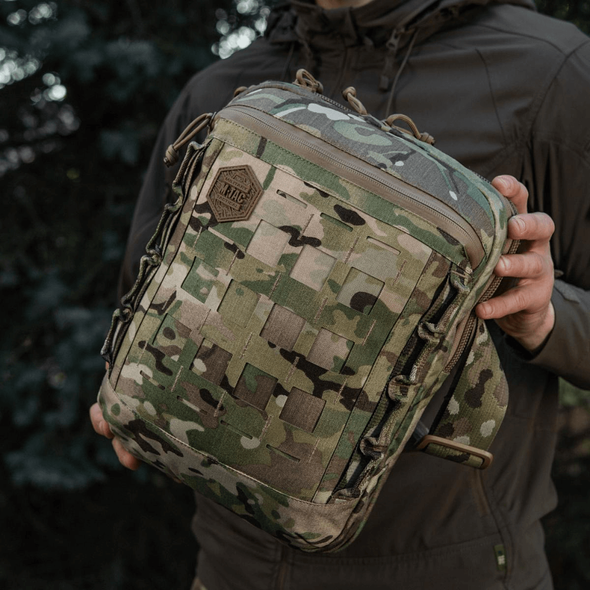 M-Tac Tablet Bag Laser Cut Hex i camo, holdt af en person, fremstillet af Cordura med Laser Cut MOLLE-panel til EDC-opbevaring.