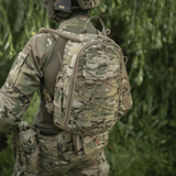 Soldat i camouflageuniform bærer taktisk rygsæk i skovområde