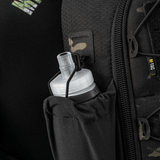 Sort rygsæk med netlomme og hvidt, rund låg til drikkeflaske, perfekt til udendørs aktiviteter. Camouflagedetaljer og lynlås synlige.