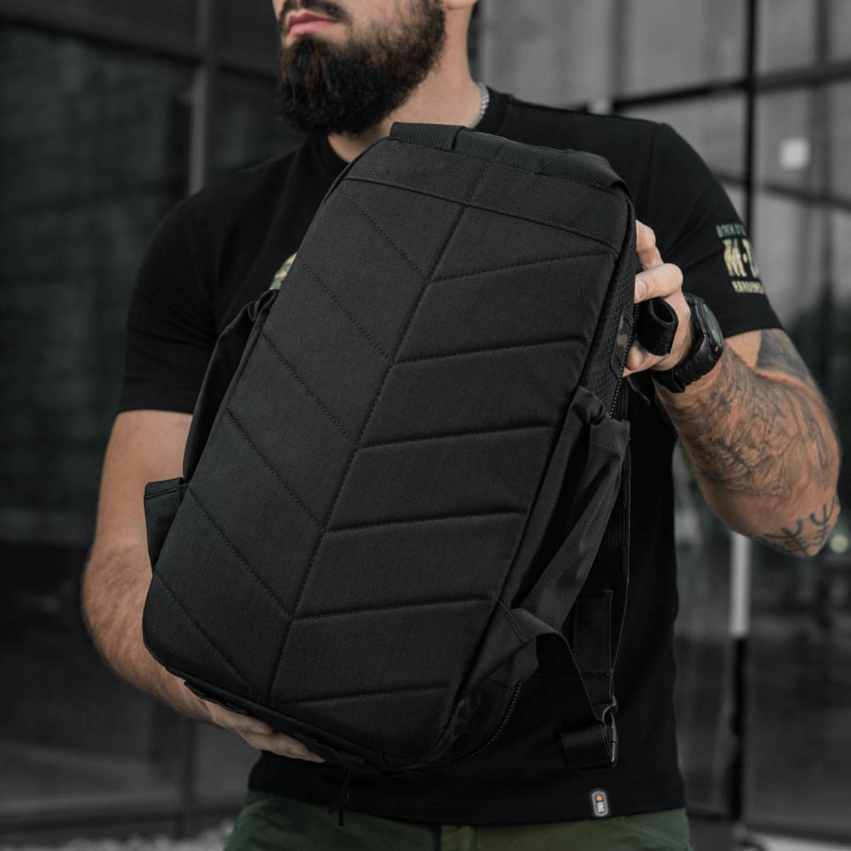 Mand viser sort rygsæk i moderne bymiljø