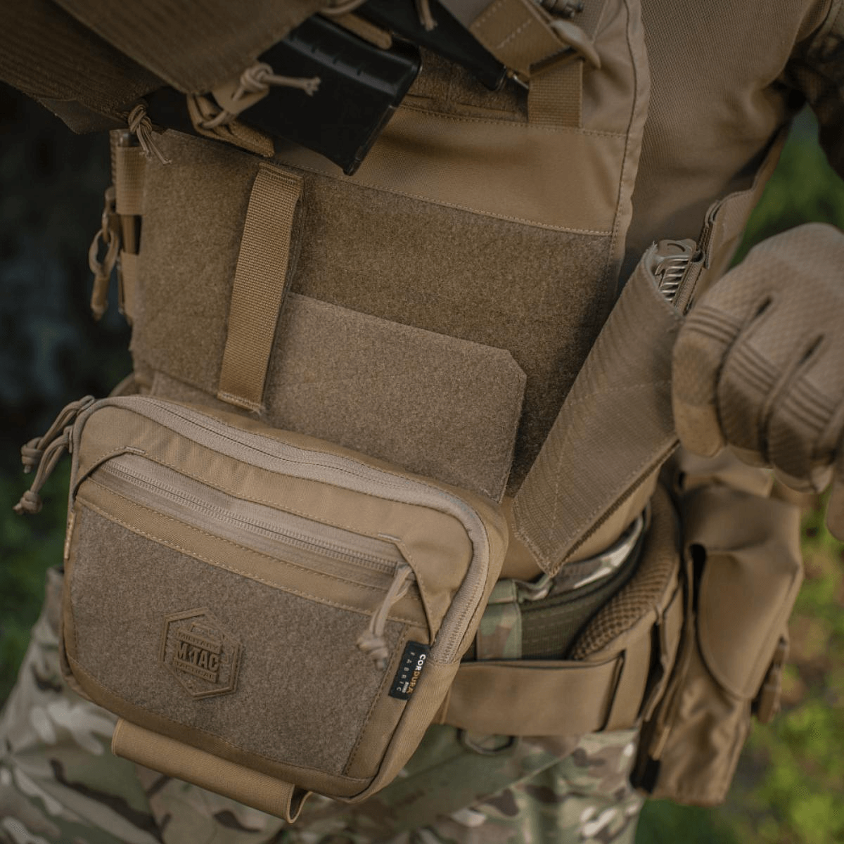 M-Tac Large Elite Gen.II Skuldertaske i Cordura 500D, perfekt til taktisk brug, med Velcro-panel og YKK lynlåse på en person i camoufleret tøj.