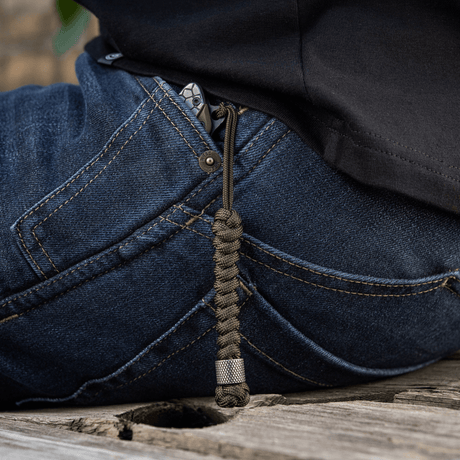 M-Tac Viper Lanyard Stainless Steel i lommen på jeans, flettet paracord med Viper-perle, fleksibel forlængelse til knivhåndtaget.