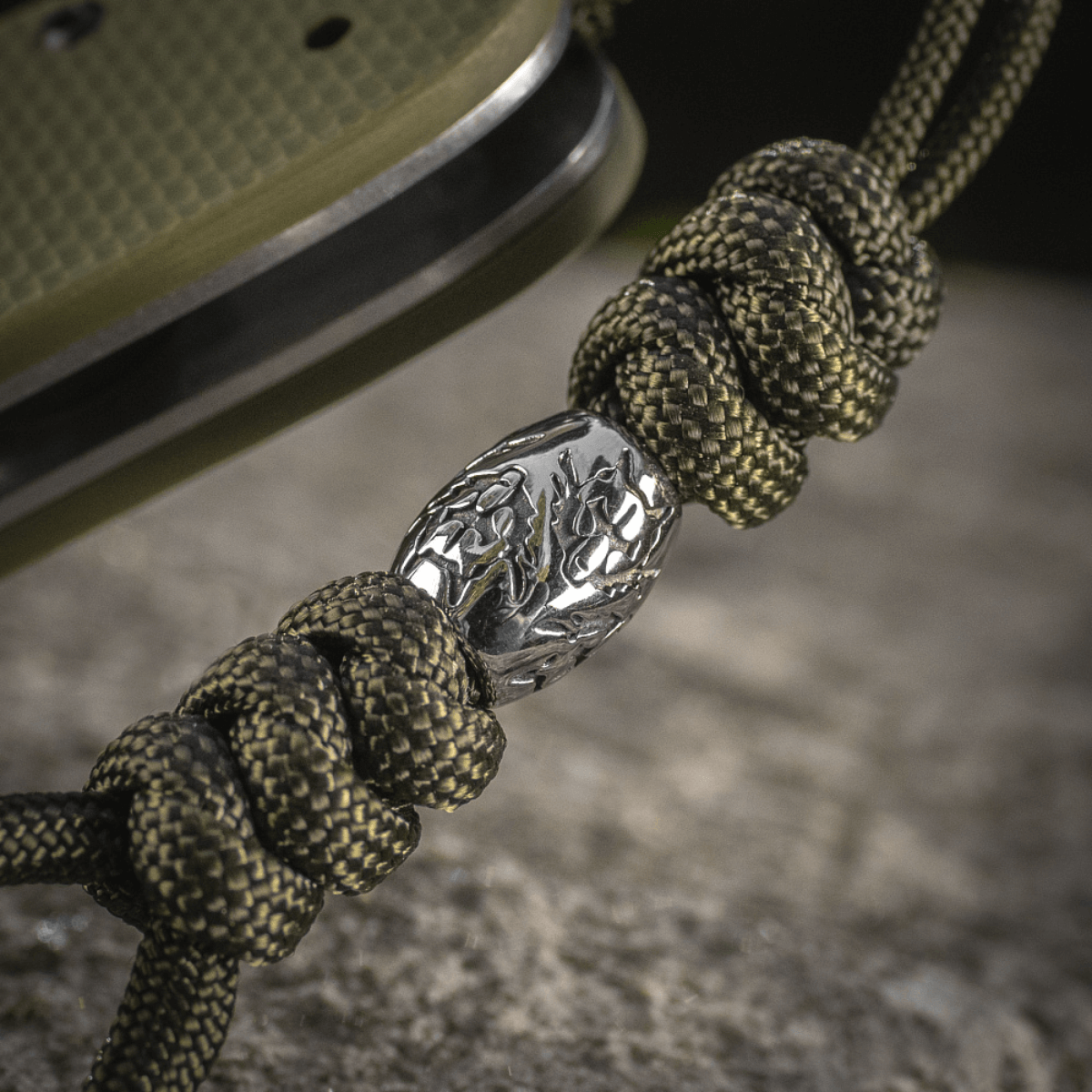 M-Tac Zeus Stainless Steel Lanyard med flettet paracord og dekorativ metalperle på en kniv, perfekt til hurtig adgang.