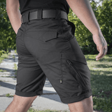 M-Tac Shorts Aggressor Gen.II Flex til alsidig brug udendørs, sort design, mand i shorts på gåtur i parkområde, let og funktionel pasform.