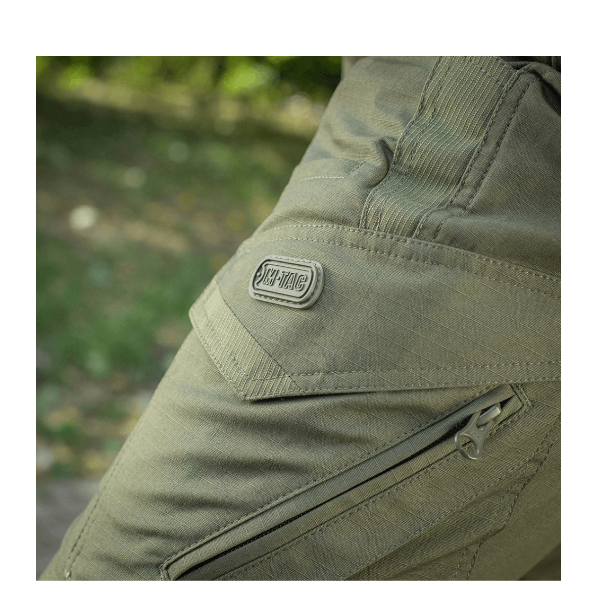 Detalje af M-Tac Bukser Aggressor Dame Flex i grønt, viser robust lynlås og logo, ideel til træning og udendørs aktiviteter.