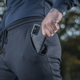 Mand tager telefon op af lommen i M-Tac Bukser Stealth Cotton med smart elastik og bevægelsesfrihed.
