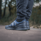 Mand bærer M-Tac Bukser Stealth Cotton under løb i parken, fremhæver komfort og stil med sort sneakers og elastik i taljen.