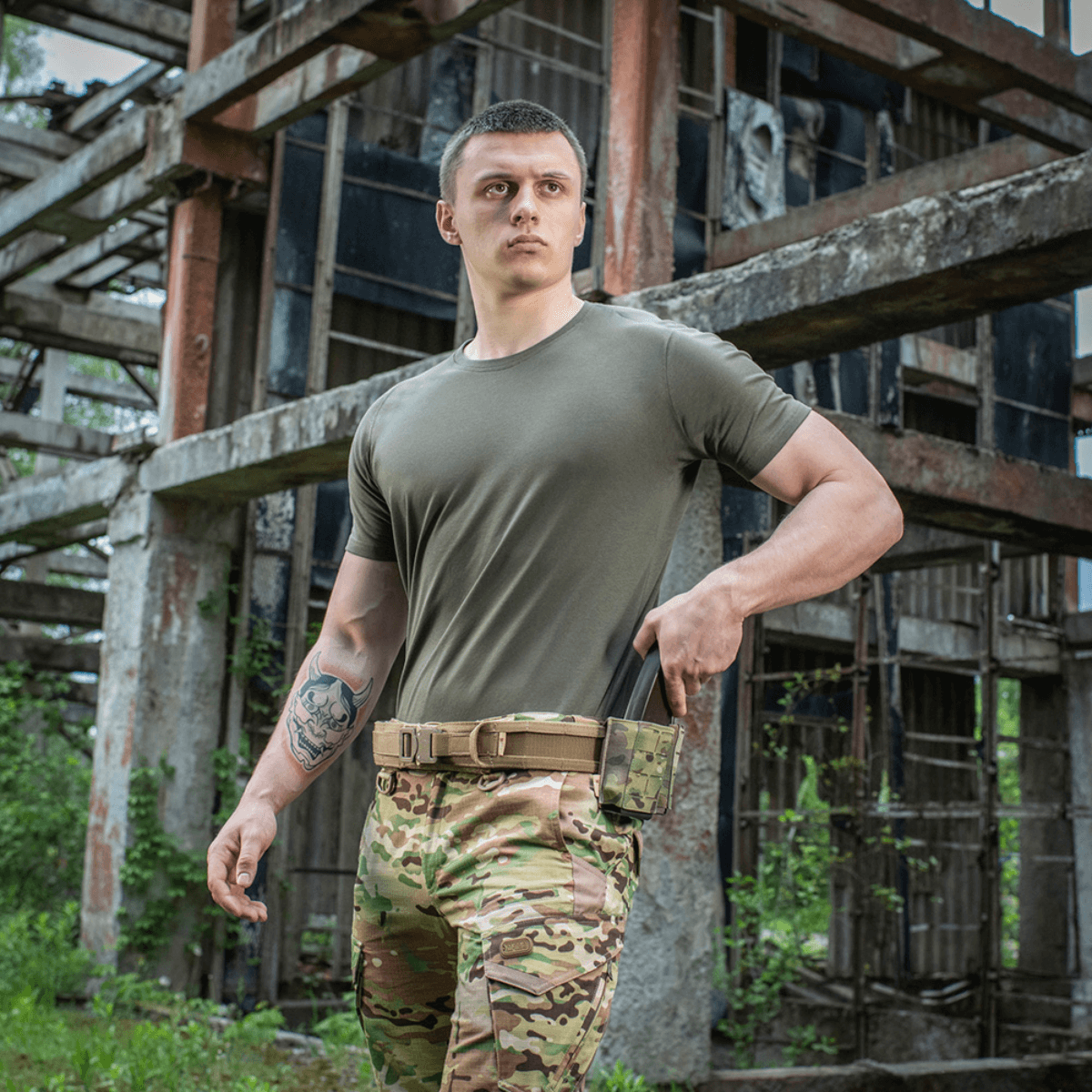 Mand iført M-Tac T-shirt 93/7 Summer ved en industriel bygning, perfekt til hverdagsbrug og sommerens varme dage.