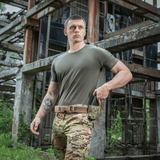 Mand iført M-Tac T-shirt 93/7 Summer ved en industriel bygning, perfekt til hverdagsbrug og sommerens varme dage.