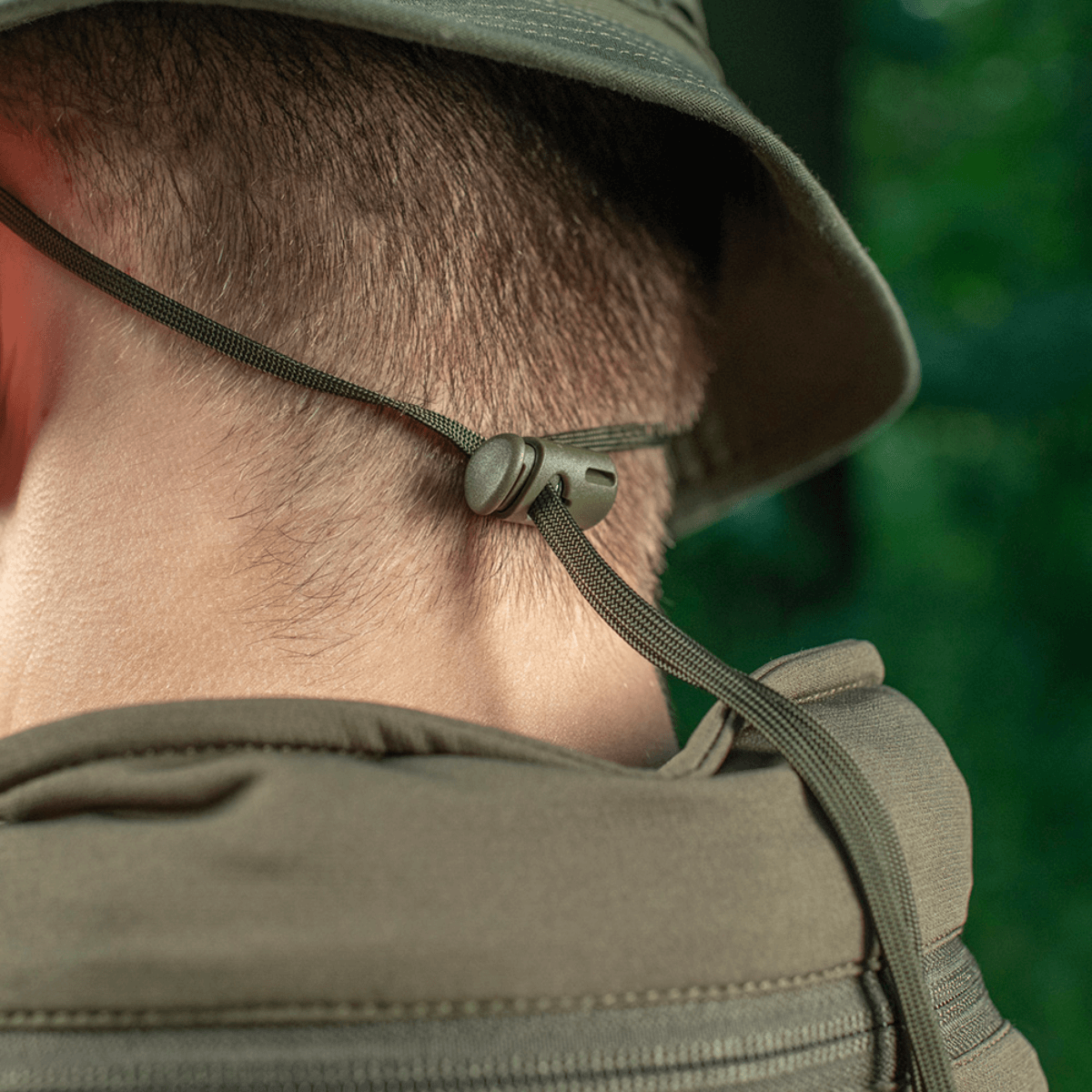 Viser bagsiden af en M-Tac Panama Rip-Stop hat, med justerbar snor for sikker pasform, set i naturmiljø.