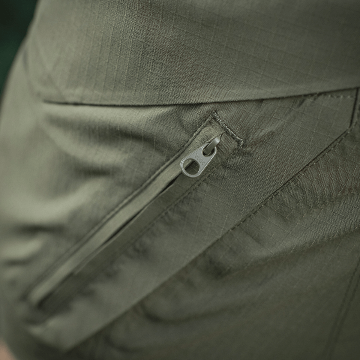 Nærbillede af lomme med lynlås på M-Tac Aggressor Summer Flex Shorts i grøn rip-stop stof.