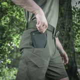 Mand iført M-Tac Aggressor Summer Flex Shorts i naturen, viser baglomme med en D-ring og robust design til udendørs aktiviteter.