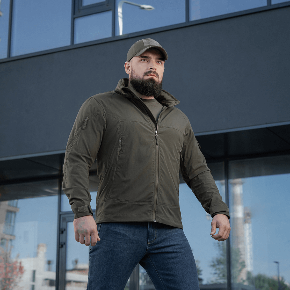 Mand iført M-Tac Flash Jakke står foran bygning, alsidig jakke til vandreture og sport, praktisk letvægtsdesign uden velcrofelter.