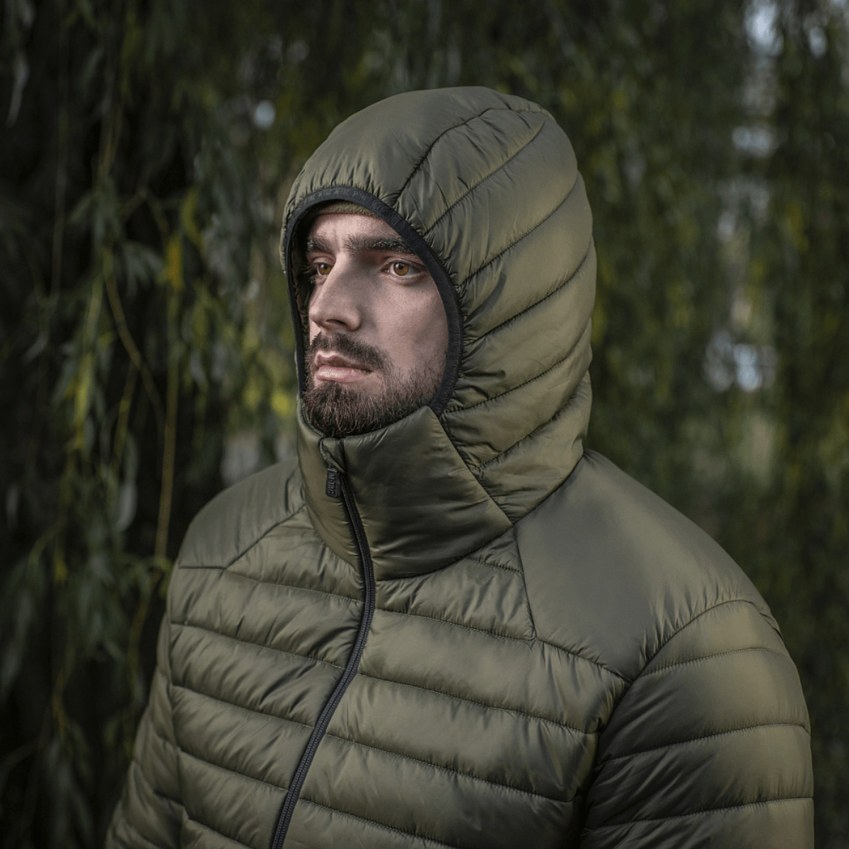 Mand iført M-Tac Stalker Gen.III Jakke med hætte i en skovklar baggrund