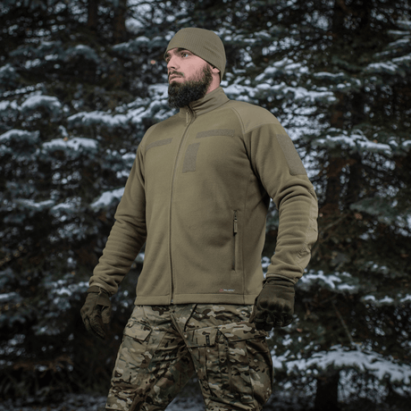 Mand iført M-Tac Combat Fleece Polartec Jakke i snedækket skovmiljø, ideel til taktisk og casual brug.