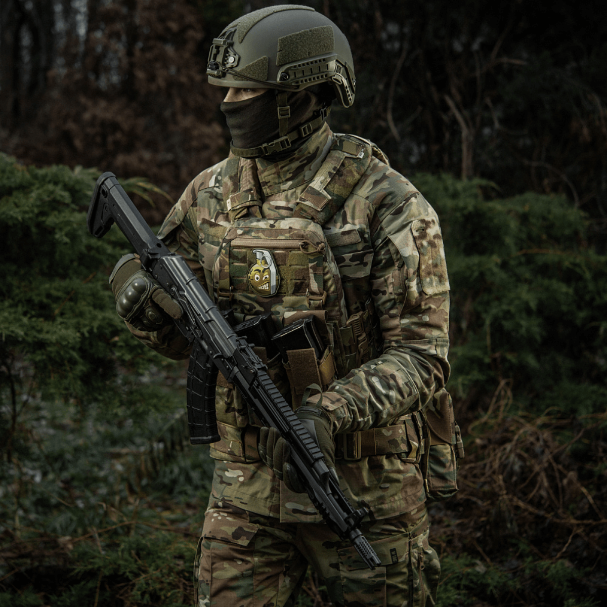En soldat i kamouflage med en M-Tac Patch M67 Granat 3D PVC på sin vest, udstyret med taktisk gear i en skovomgivelse.